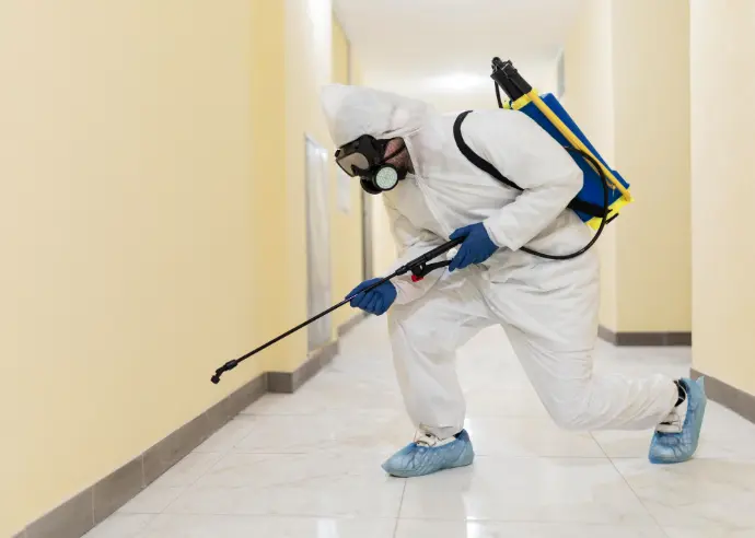 Técnico de fumigação com fato de proteção a aplicar produto num corredor